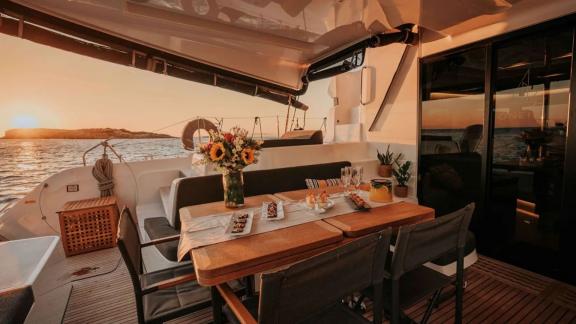 On the Oneida 2 catamaran, snacks and flowers are placed on the table at sunset.