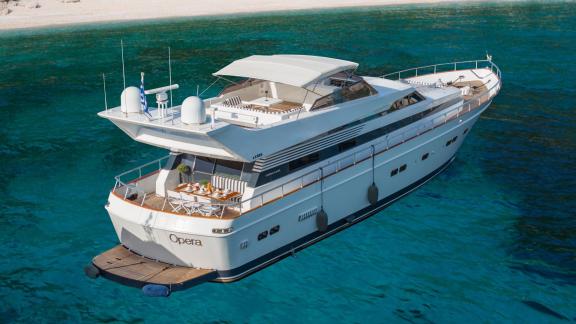 The Opera yacht is anchored in a bay, offering a comfortable seating area on the aft deck.