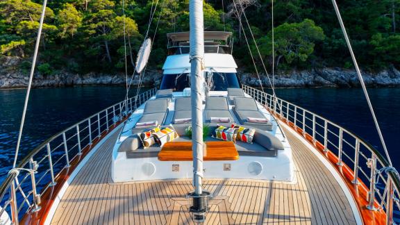 Comfortable sun loungers on the foredeck of a sailing yacht with views of the sea and coastline.