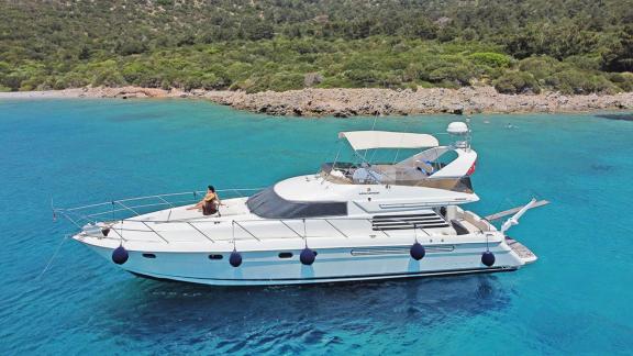 The motor yacht Queen is anchored in a serene bay, surrounded by stunning turquoise waters.