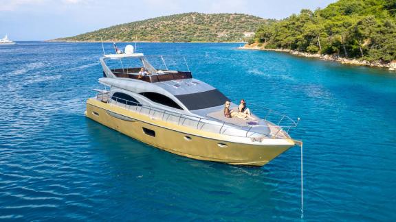 The motor yacht Selenge is anchored in a quiet bay, with two people relaxing on deck, enjoying the blue waters.