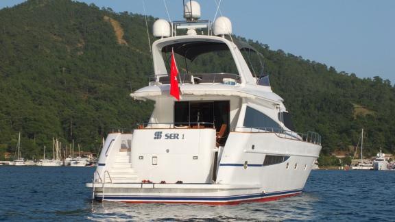 The rear of motor yacht Ser 1 with a Turkish flag against a forest backdrop.