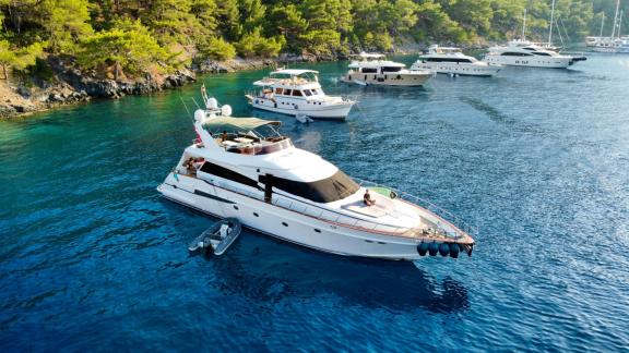 Motor yacht Ser 1 is anchored in a cove with other boats and a forest backdrop.