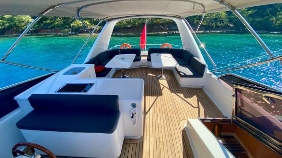 The flybridge of motor yacht Ser 1 with a comfortable seating area, overlooking a wooded cove.