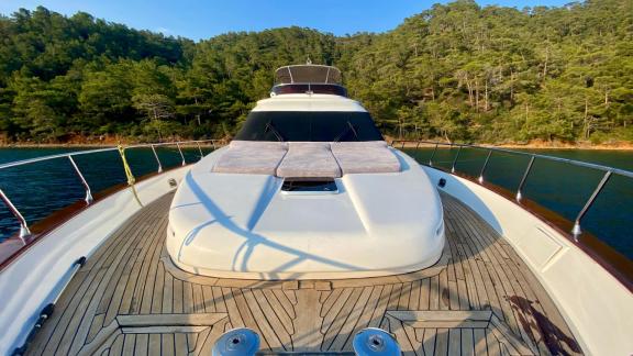 The foredeck of motor yacht Ser 1 with a sunbathing area, anchored in a wooded cove.