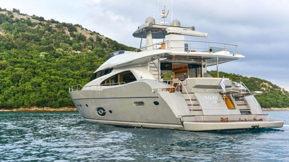 Stela 117 yacht rests calmly on the water with a lush green backdrop.