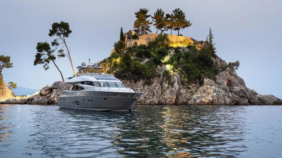 Stela 117 yacht anchored peacefully in front of a lit-up island.