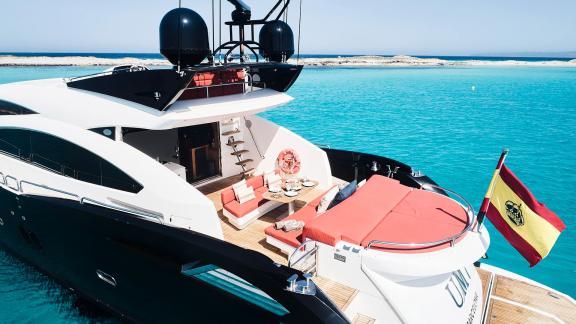 The aft deck of motor yacht Um7 features a comfortable seating area with red cushions and a sunbathing area.