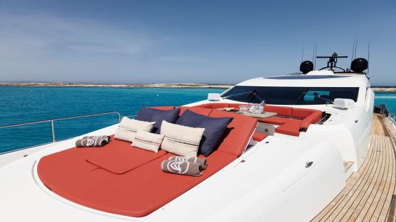 The foredeck of motor yacht Um7 features a comfortable sunbathing area with red cushions and pillows.