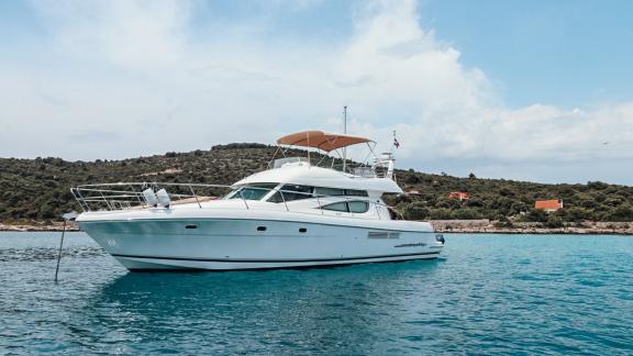 The motor yacht Unplugged anchored near the shore with a natural backdrop.