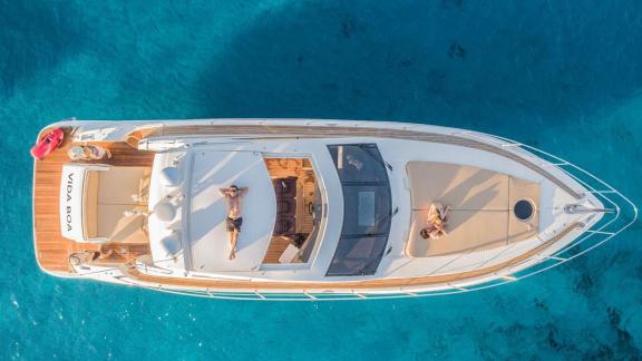 Guests enjoy sunbathing on the spacious deck of motor yacht Vida Boa over turquoise waters.