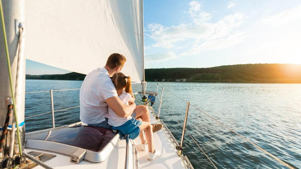 Ein Vater umarmt sein Kind auf dem Deck einer Segelyacht, während sie den Sonnenuntergang über dem Meer genießen.