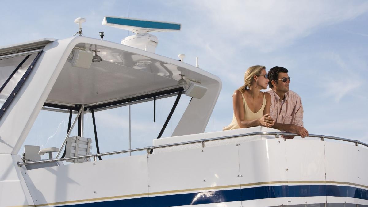 A couple sits on the deck of the white luxury yacht which they have rented and enjoys the blue ride.