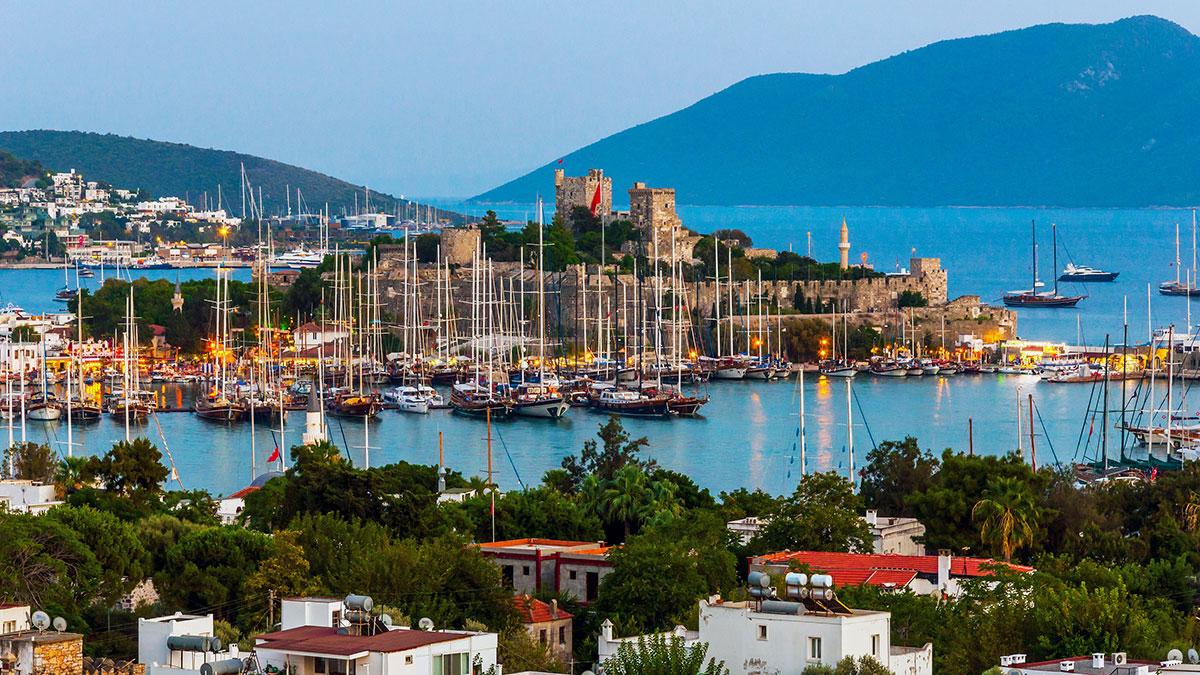 A picturesque harbor at dusk with yachts and a striking medieval castle in the background