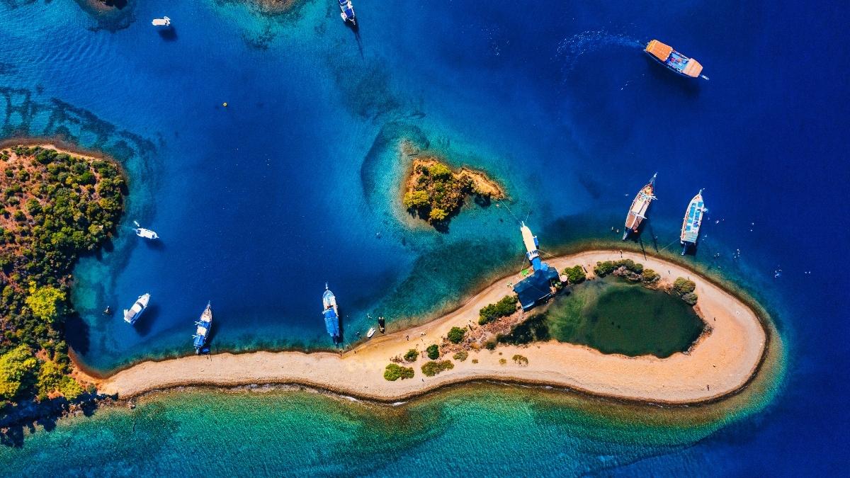 Aerial view of multiple gulets anchored around a sandy peninsula and small islands in Göcek, Turkey