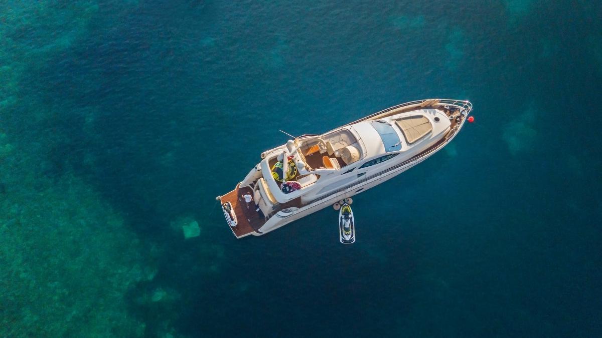 Luxusyacht in türkisfarbenem Wasser, mit angebundenem Jetski, von oben gesehen