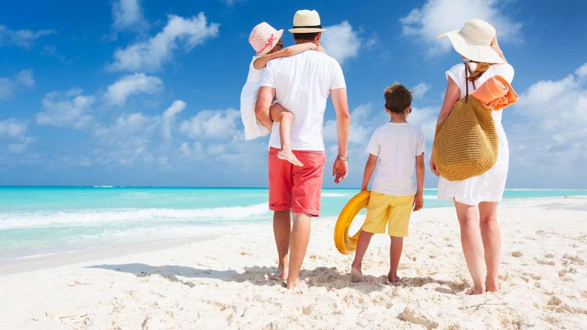 Семейная пара с двумя детьми гуляет по песчаному пляжу и смотрит на море