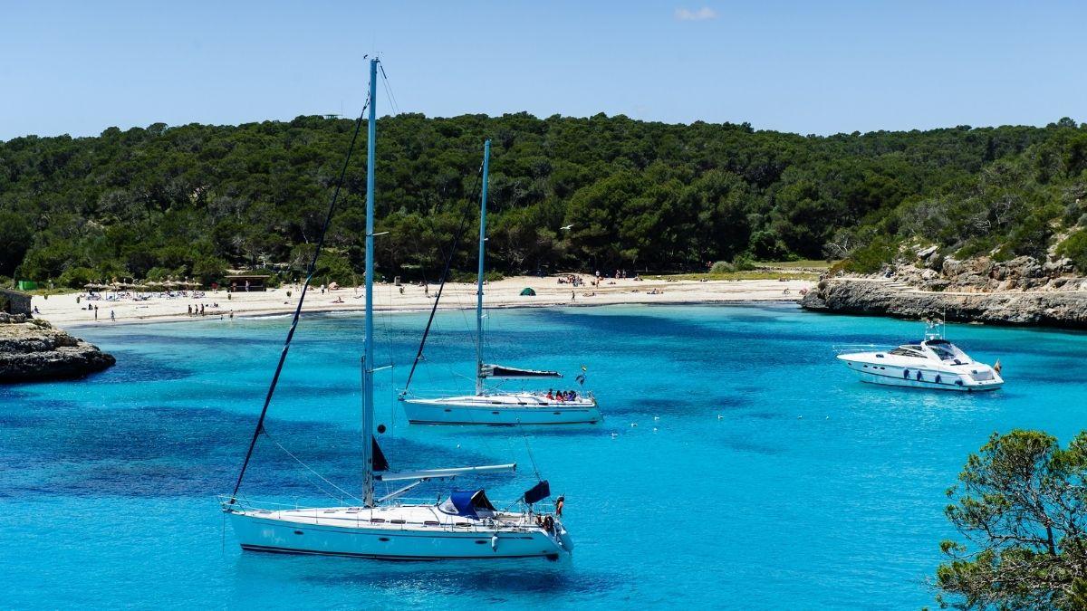 Mehrere Yachten ankern im kristallklaren blauen Wasser vor einer bewaldeten Küste in der Türkei.