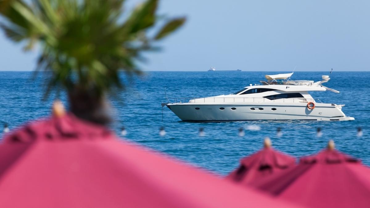 A stylish motor yacht cruising near the coast, with blurred beach details in the foreground.