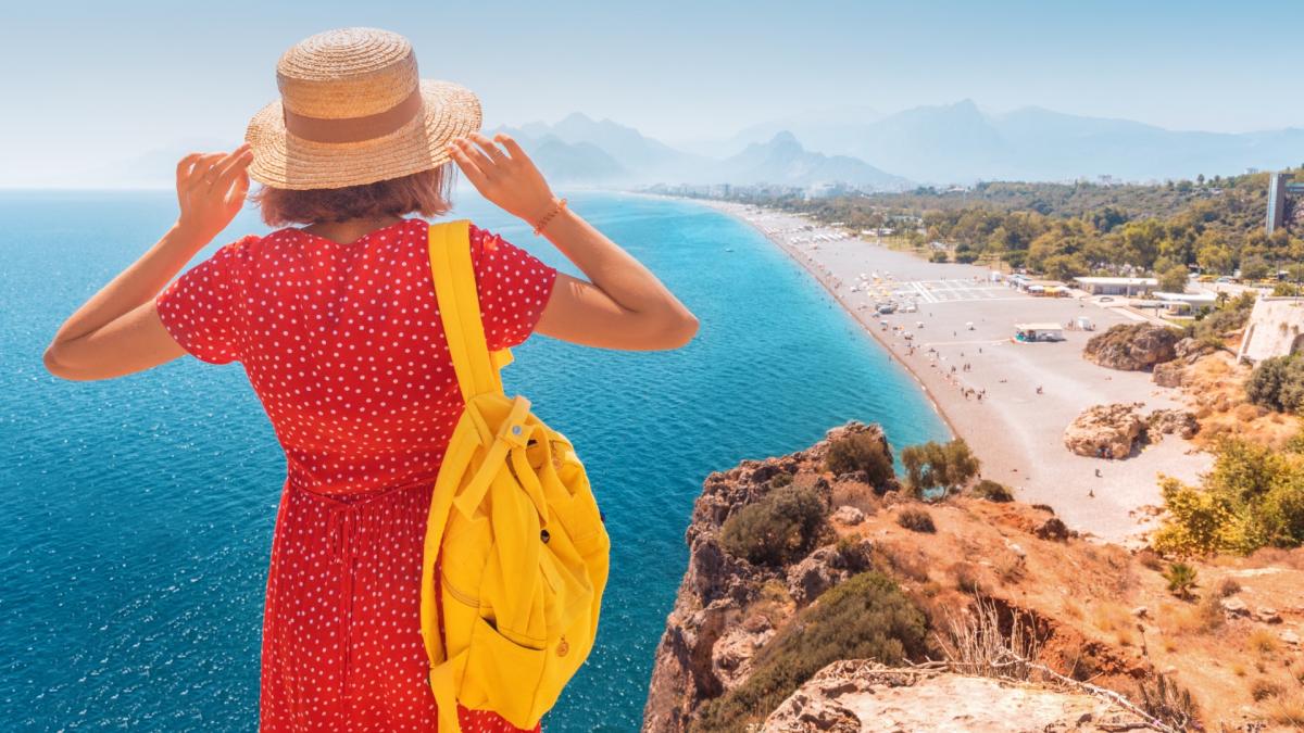 Frau in rotem Kleid und Strohhut genießt die Aussicht auf das Meer und den Strand.