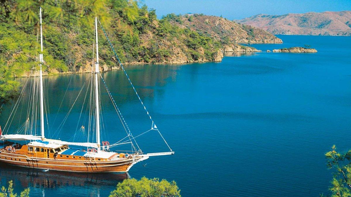 Eine wunderschöne Gulet-Yacht ankert in einer ruhigen Bucht, umgeben von grünen Hügeln und blauem Wasser