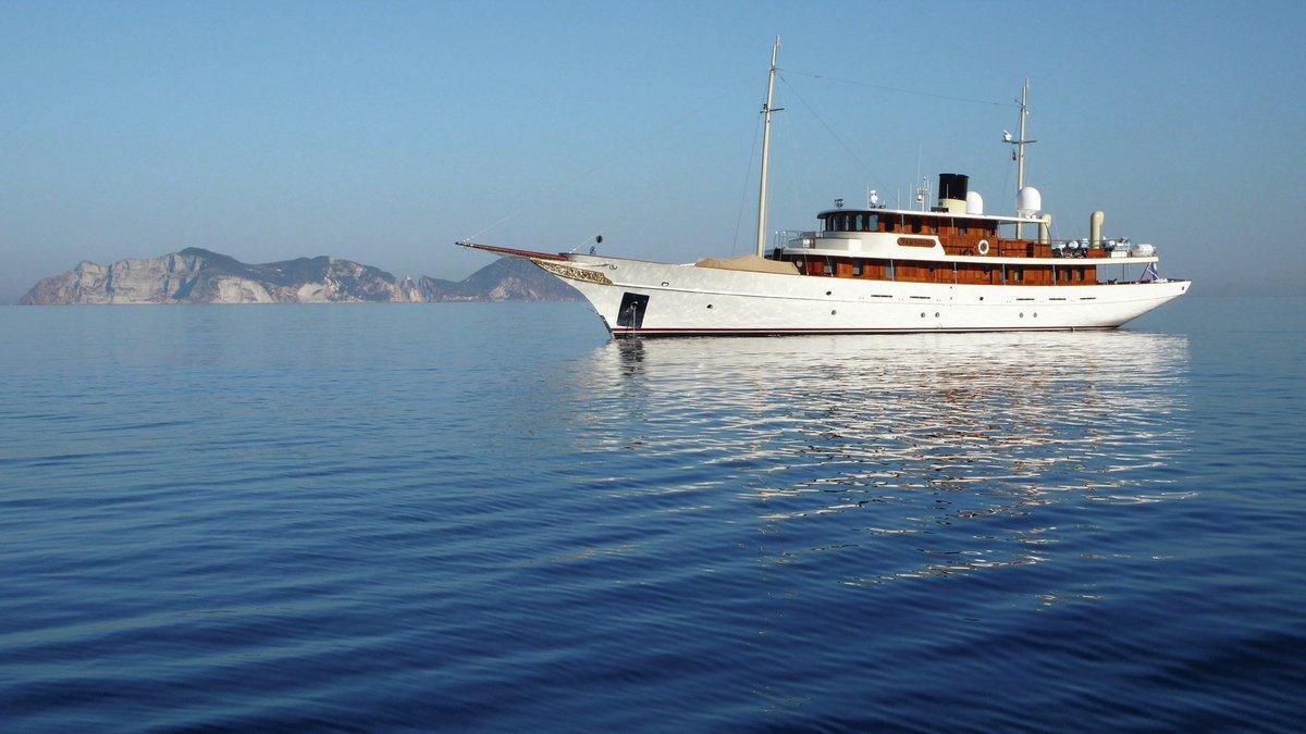 A magnificent yacht glides on calm waters with a distant island in the background