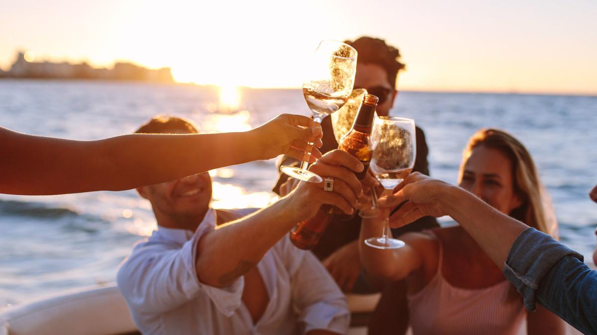 Vier Personen stoßen mit Wein auf einer Motoryacht im Meer an, während die Sonne untergeht