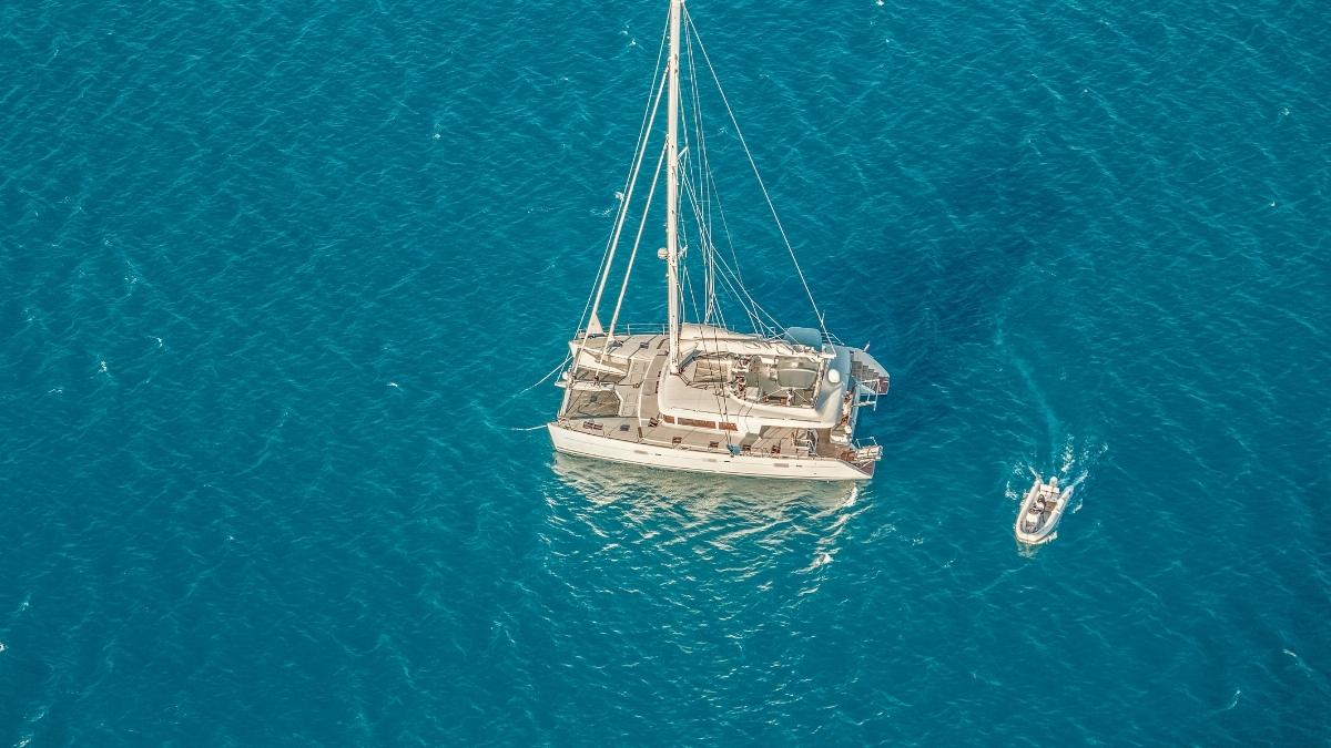 Aerial view of a catamaran and a small dinghy on clear, deep blue water.