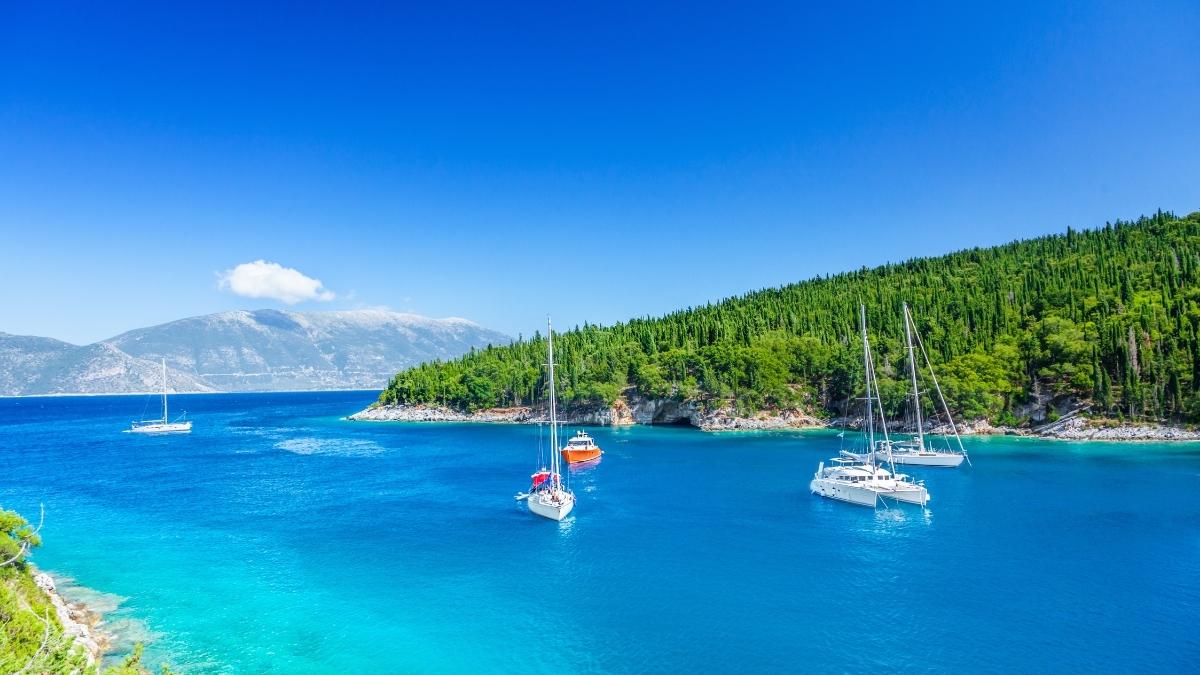 Greece Yacht Charter: yachts anchored in turquoise waters, framed by lush green hills and distant mountains.