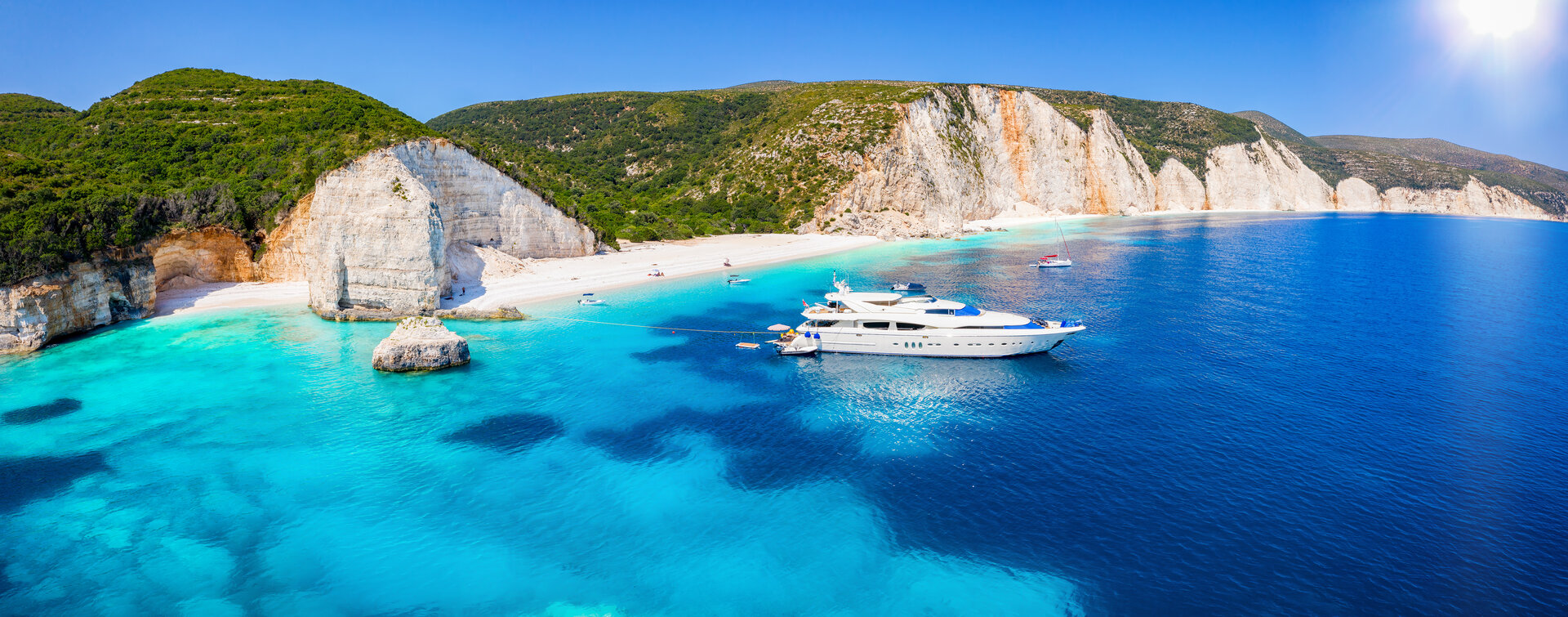 Weiße Yacht im türkisfarbenen Wasser vor steilen Klippen, ideal zum Boot mieten in Lefkada