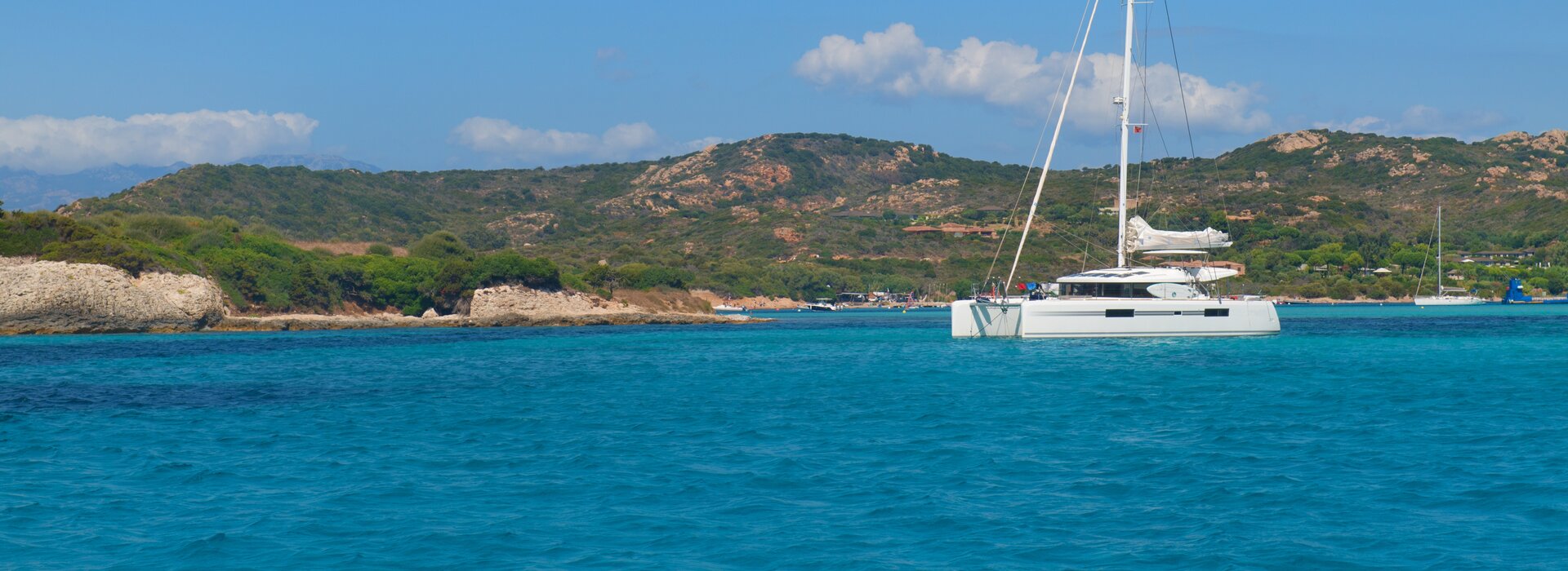 Modern white catamaran charter Palairos anchored in crystal clear turquoise waters near a scenic coastline