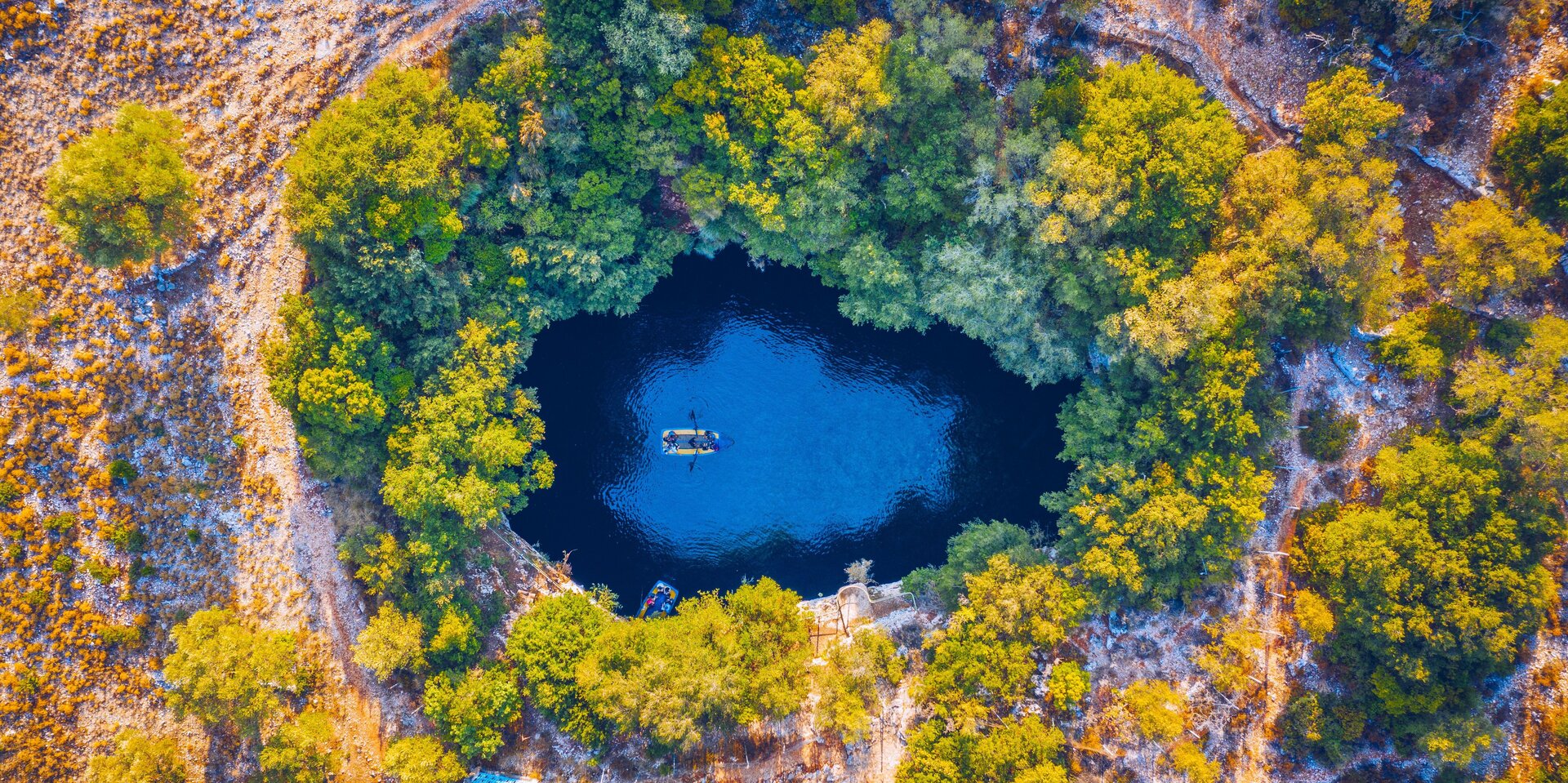 Luftaufnahme der Melissani-Höhle bei einem Katamaran Charter Sami, kristallblaues Wasser umgeben von grüner Natur