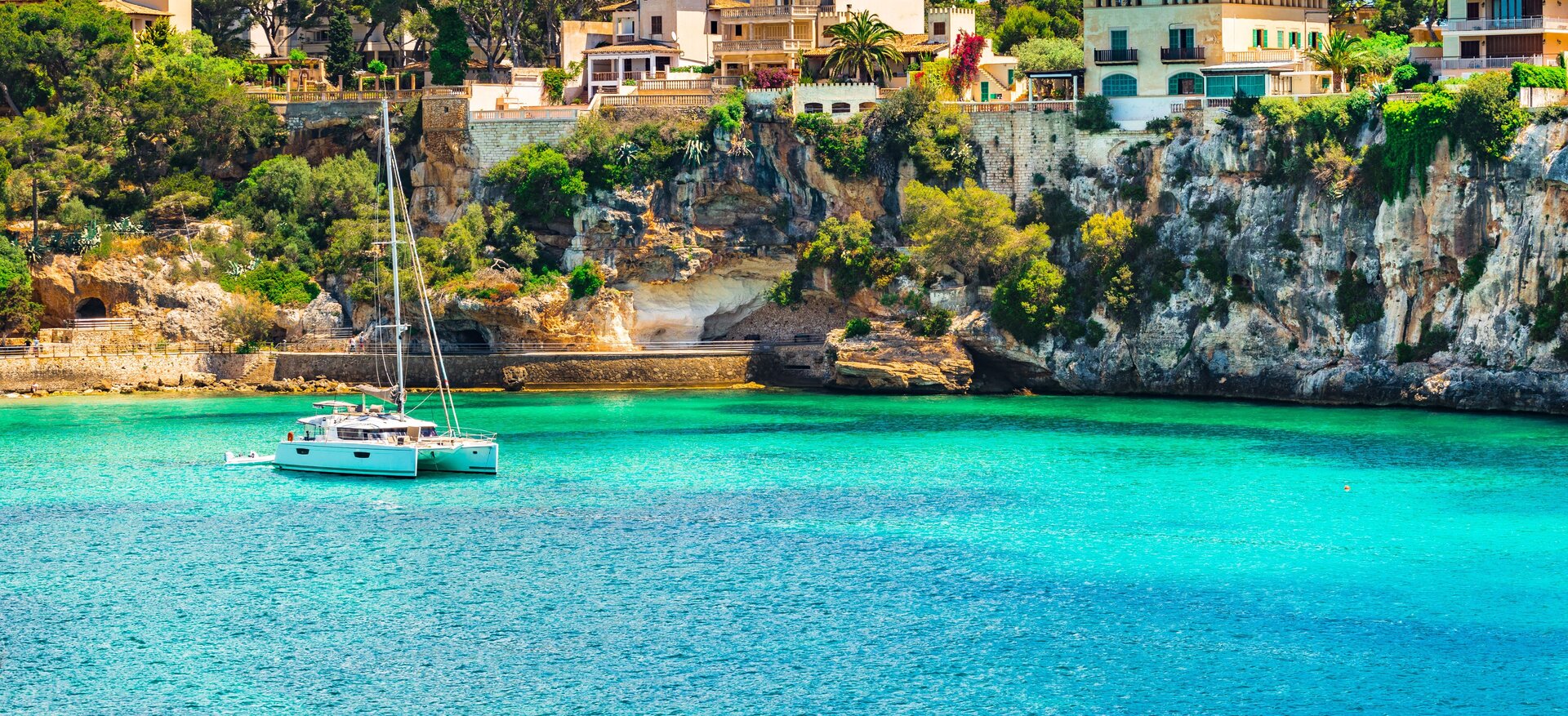 Scenic view of a white sailing vessel anchored during a catamaran rental in turquoise water near a rocky coastline