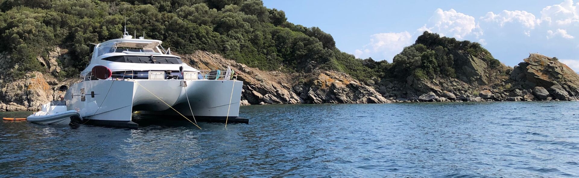 Bembeyaz bir katamaran, bulutsuz gökyüzü altında masmavi denizde huzurla yüzüyor