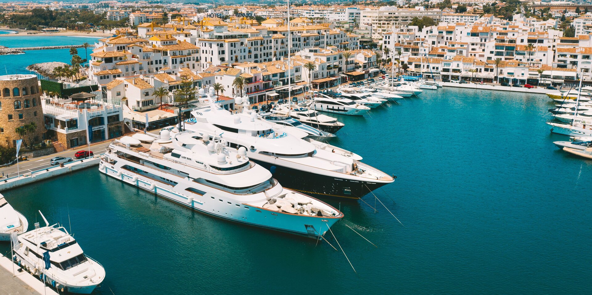 Blick auf eine Reihe exklusiver Charteryachten, die im sonnigen Hafen vor einer mediterranen Stadtkulisse liegen