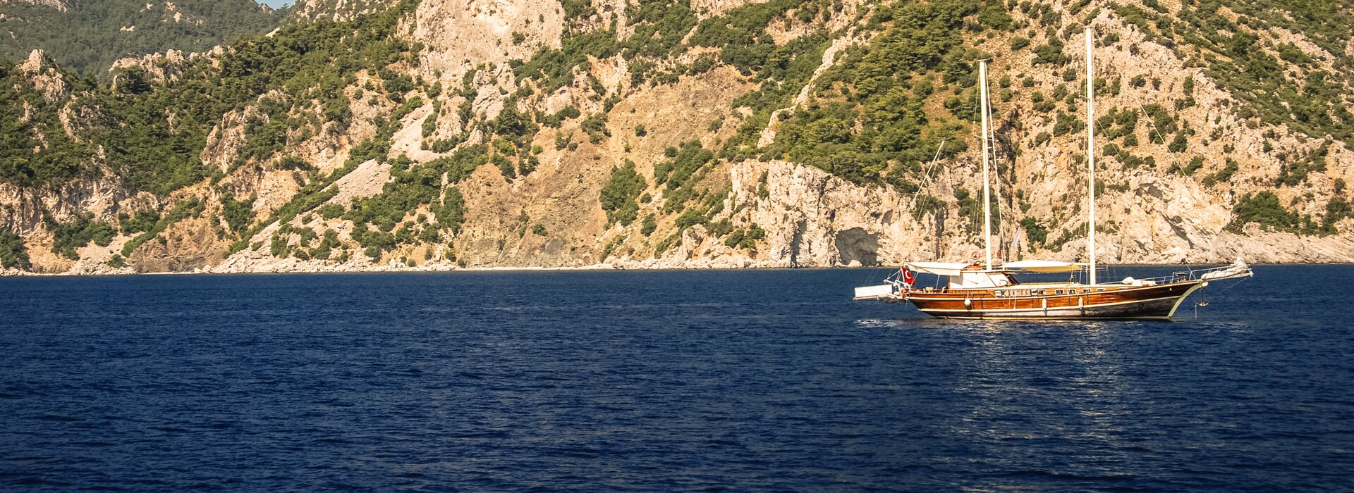 Eine hölzerne Gulet ankert vor einer felsigen Steilküste, ideal für einen Gulet Charter Italien