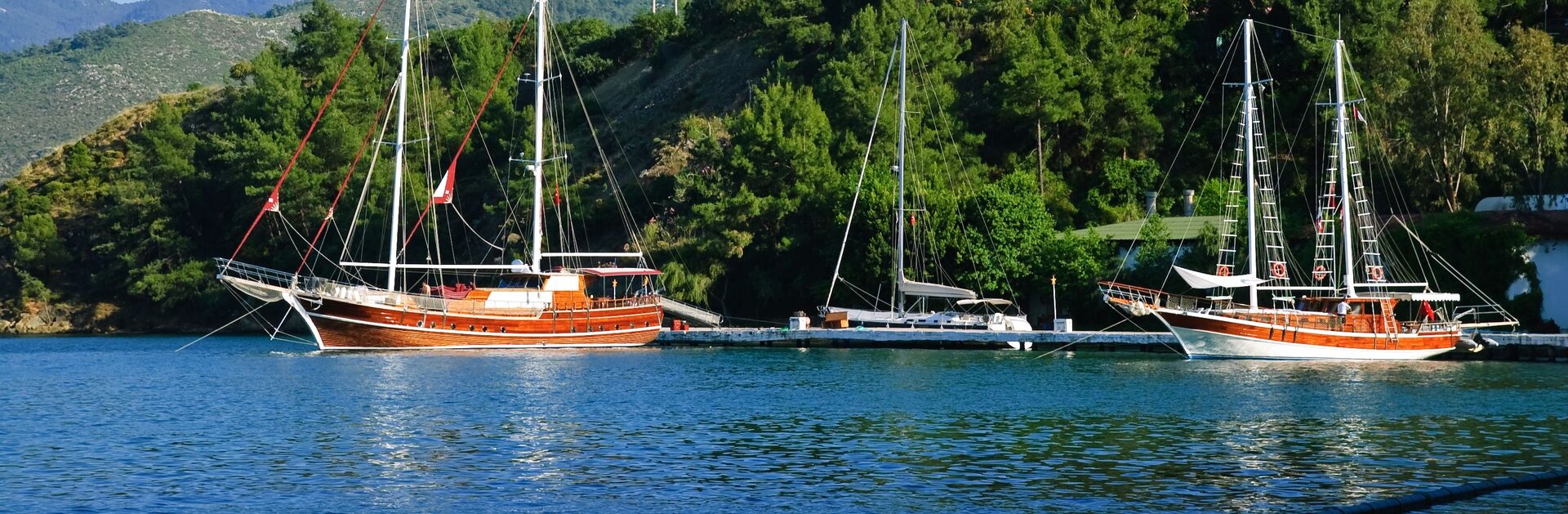 Zwei traditionelle Gulets liegen an einem Steg vor bewaldeter Küste, die Auswahl beim Gulet Charter in Athen