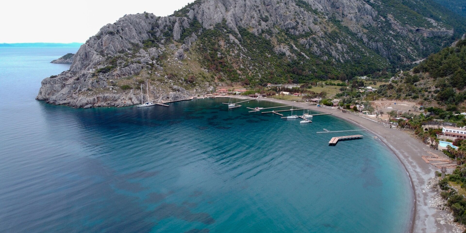 Marmaris Çiftlik Koyu'nda sarp kayalıklar önünde demirlemiş yelkenli tekneler ile Marmaris yelkenli kiralama