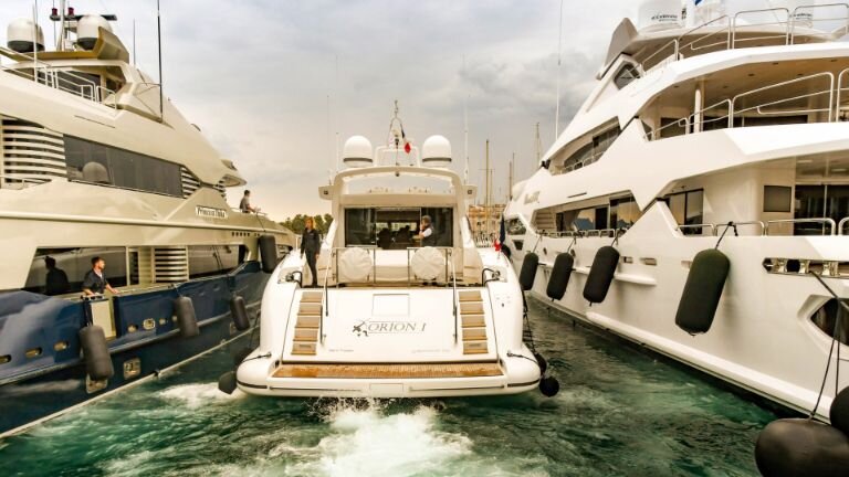 Bir motoryat, iki süperyat arasında limana geri manevra yapıyor