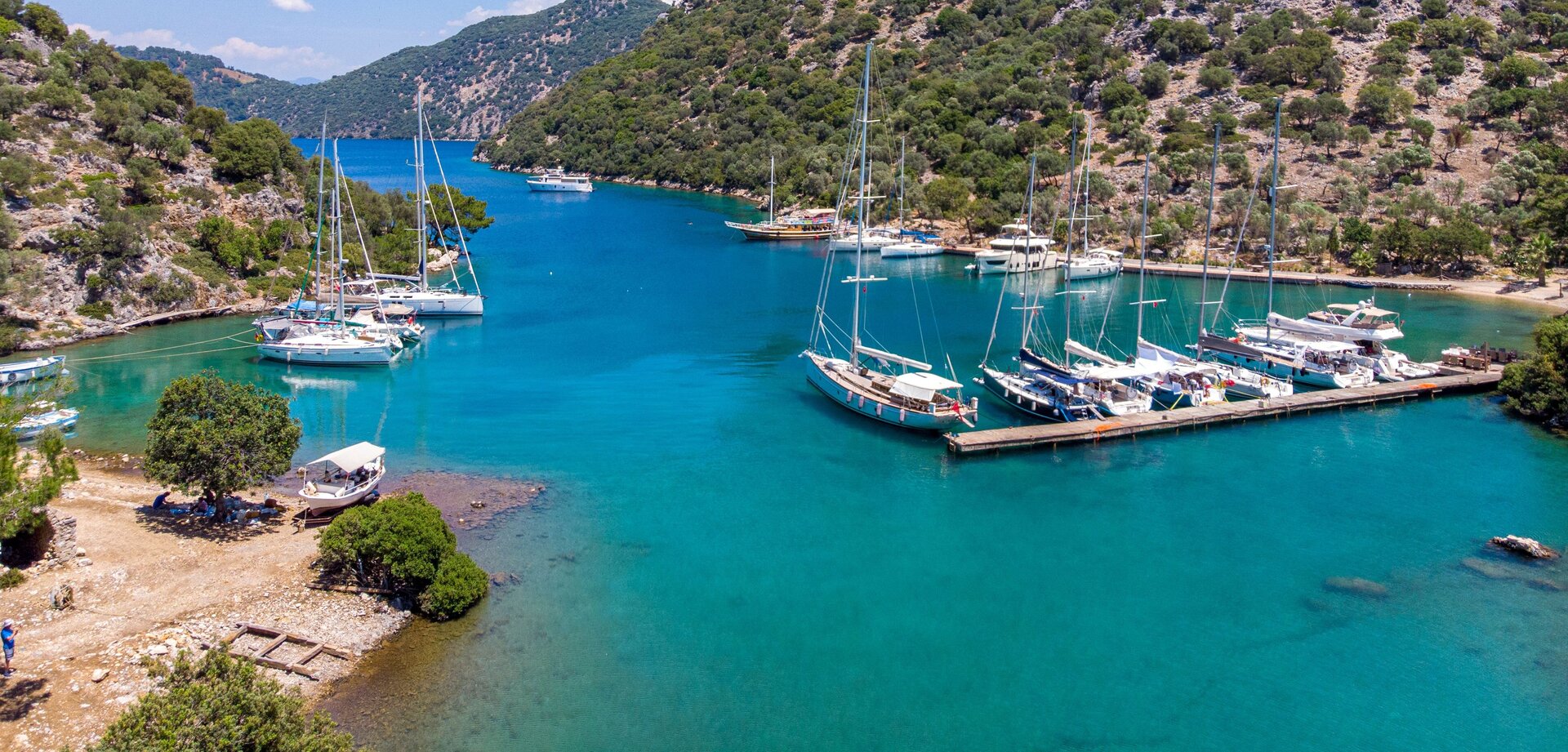 Motorsegler und Yachten an einem Holzsteg in einer grünen Bucht beim Motorsegler in Fethiye mieten