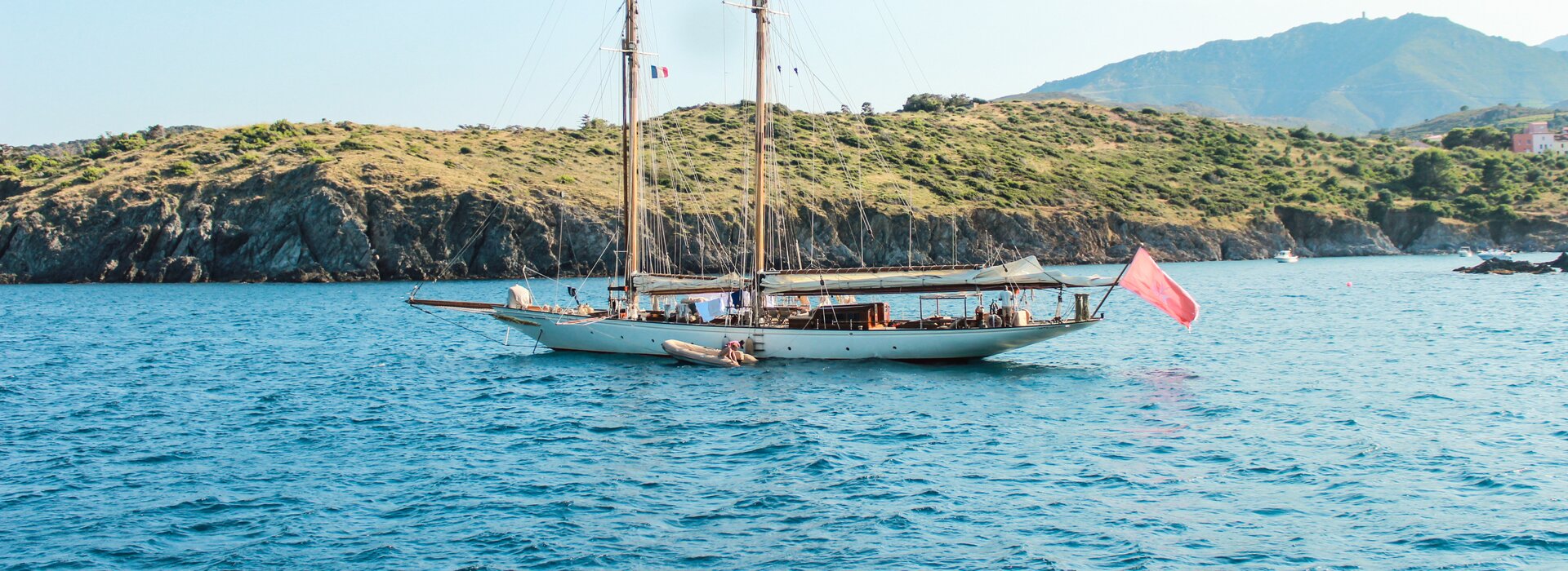 Ein traditionelles Zwei-Mast-Gulet mit roter Flagge vor felsiger sardischer Küste, perfekt für einen Gulet Charter Olbia