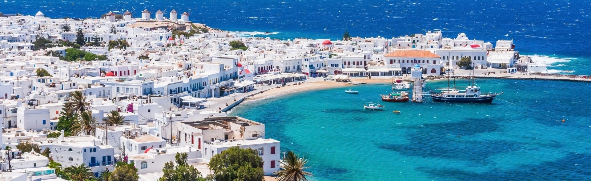 Вид на город Миконос с белыми домами, ветряными мельницами и маленькой гаванью с яхтами на бирюзовом море