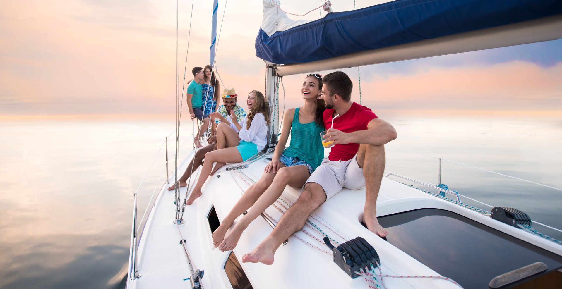 Gün batımında güvertede eğlenen bir grup arkadaş, Hırvatistan'da yelkenli kiralama keyfinin en güzel anı