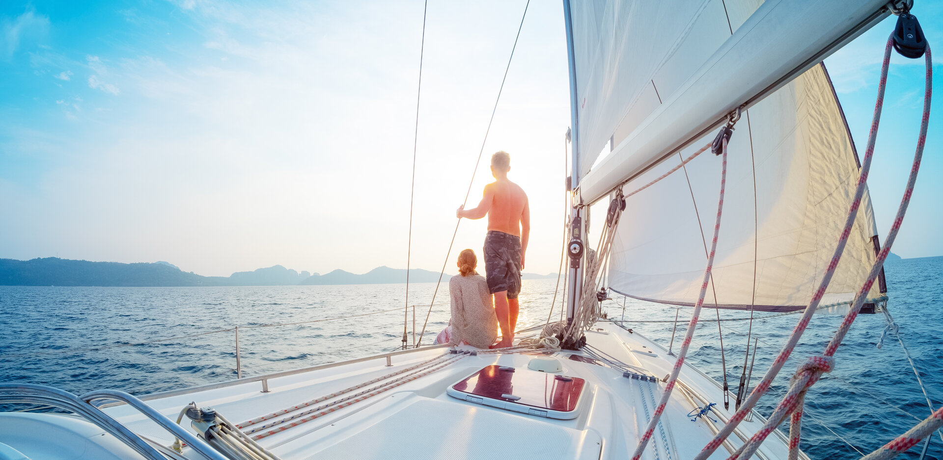 Luftaufnahme eines Paares auf dem Vordeck, die ein Segelboot mieten Lavrion und in den Sonnenuntergang steuern