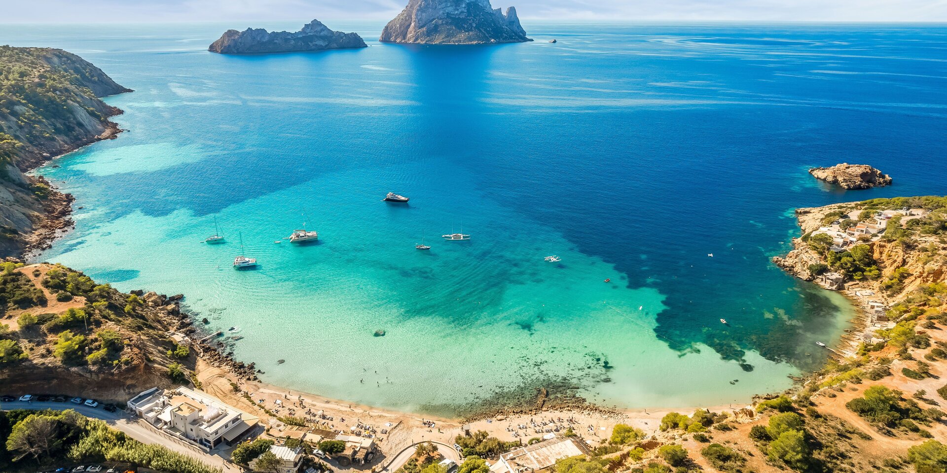 İbiza'daki Cala d'Hort koyunun yat kiralama seçenekleri ve arka planda Es Vedrà adası ile havadan görünümü