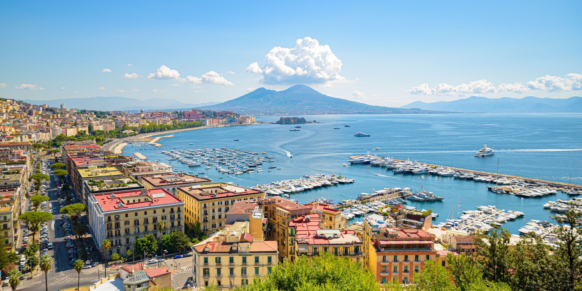 Stadtpanorama von Neapel mit dem Vesuv und dem Hafen voller Schiffe, der ideale Startpunkt für einen Yachtcharter Neapel